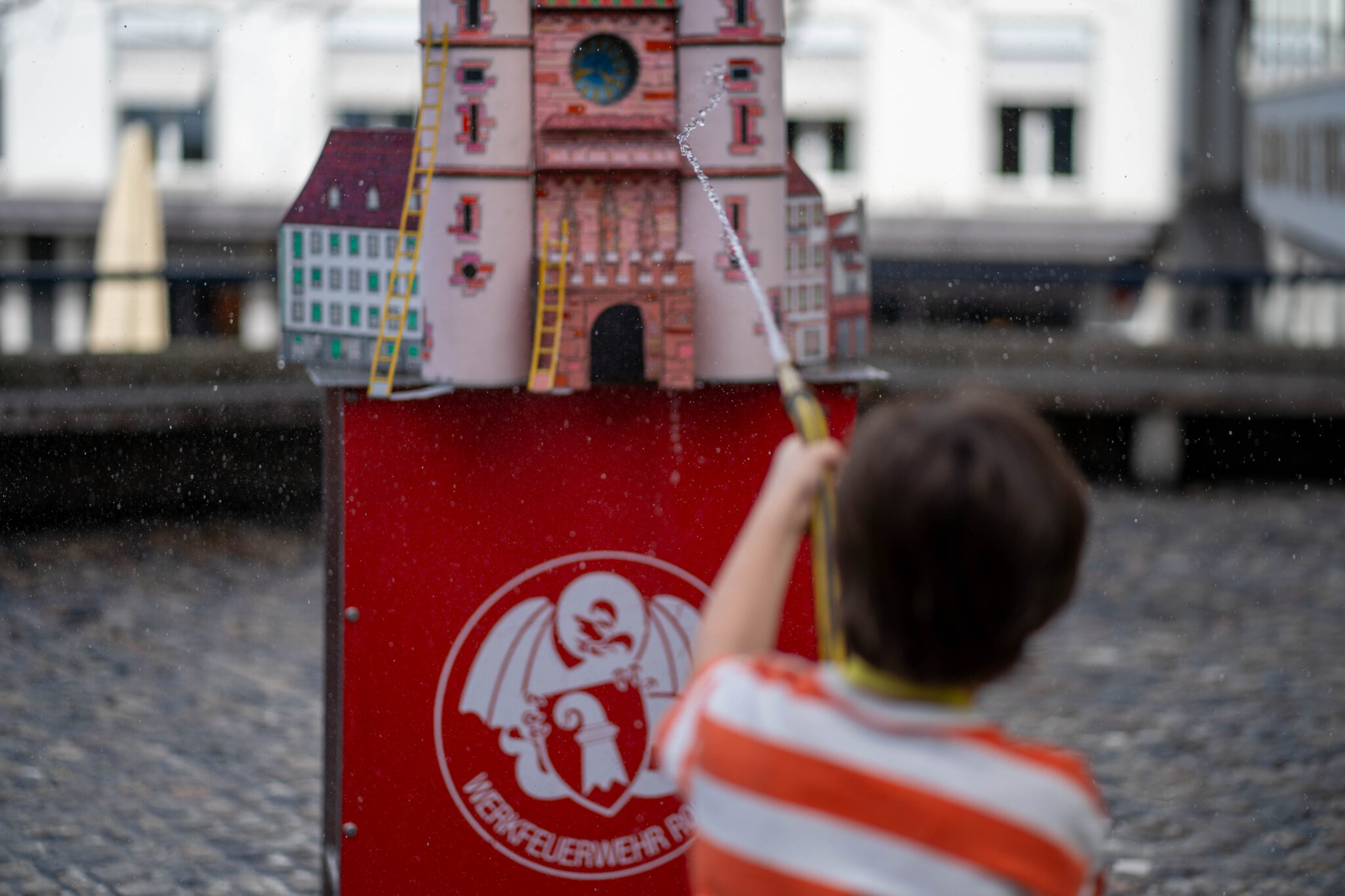 Ein Kind spritzt mit einem Schlauch Wasser auf ein modelliertes Spalentor.