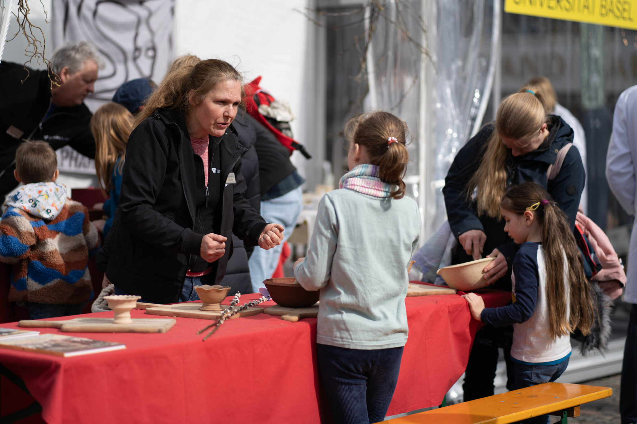 Zwei Kinder mit langen Haaren stellen mit Hilfe von zwei Erwachsenen Räuchermischungen her. Sie stehen an einem Tisch mit einem roten Tischtuch. Darauf stehen Tonschalen.