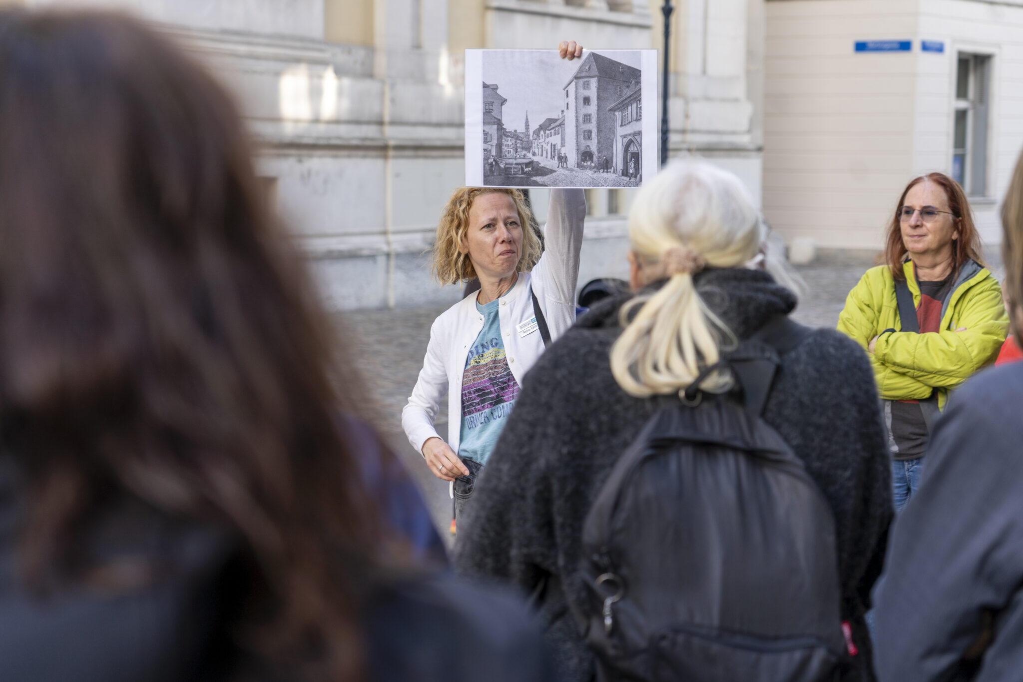 Eine Frau streckt ein schwarz-weiss Bild in die Luft. Sie zeigt es einem Publikum, das vor ihr steht.