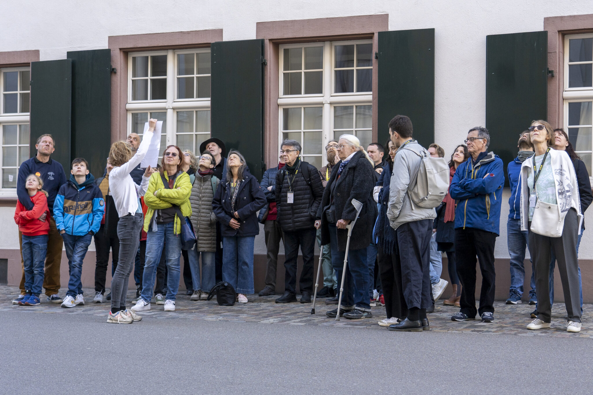 Eine Frau streckt ein schwarz-weiss Bild in die Luft. Sie zeigt es einem Publikum, das vor ihr steht.